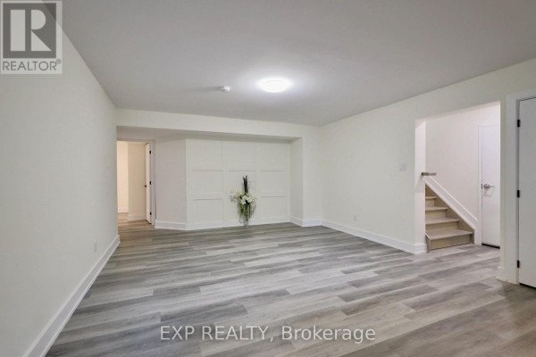 Empty basement living area with light grey wood-look flooring and white walls. - B - 12 Sylvester Street, Ottawa
