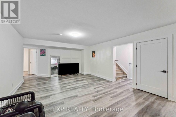 Basement living area with a large television, staircase, and white panel wall. - B - 12 Sylvester Street, Ottawa