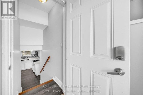 Entrance hallway showing a white door, stairs going down, and a glimpse of a kitchen. - B - 1896 Featherston Drive, Ottawa