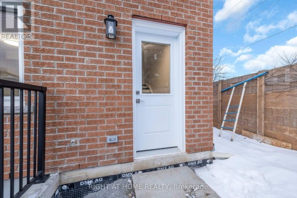 Rear exterior brick wall with a white door, black railing, and a ladder against a concrete fence. - B - 23 Kirkham Drive, Ajax