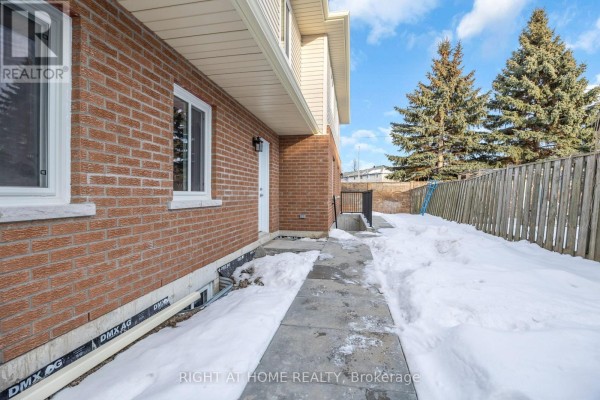 Concrete walkway beside a brick house with snow on the ground and tall evergreen trees. - B - 23 Kirkham Drive, Ajax