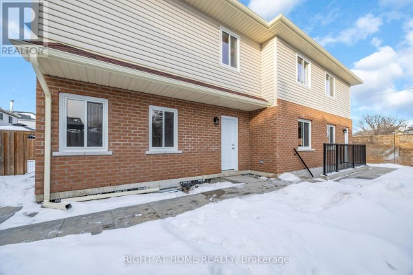 Side and rear exterior of a brick and vinyl house with snow and a wooden fence. - B - 23 Kirkham Drive, Ajax