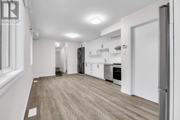 Modern white kitchen with stainless steel appliances, stacked washer and dryer, and light wood flooring. - B - 23 Kirkham Drive, Ajax