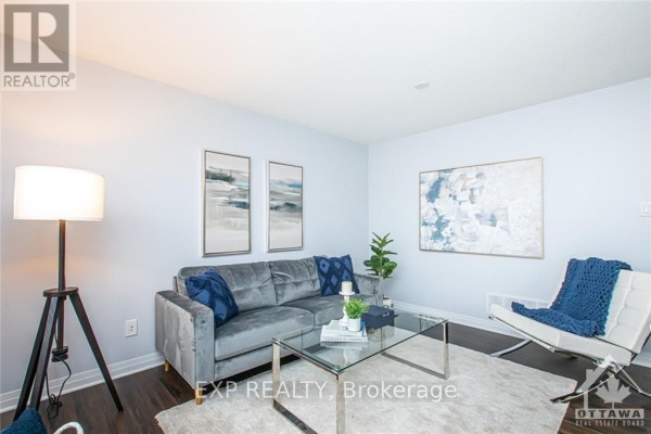 Living room with a grey sofa, glass coffee table, and a white armchair with blue throw. - B - 444 Via Verona Avenue, Ottawa