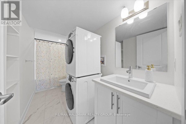 Bathroom with white vanity, sink, stacked washer and dryer, toilet, and shower curtain. - B - 525 Tahoe Heights, Ottawa