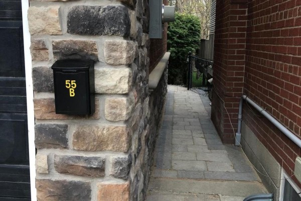 Black mailbox with yellow numbers '55 B' mounted on a stone pillar next to a paved walkway. - B - 55 Addington Avenue, Toronto