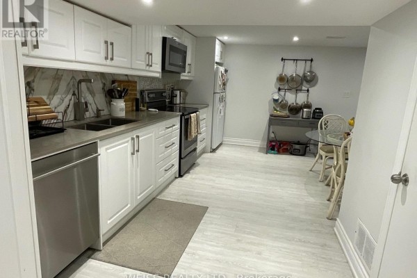 A white kitchen with grey wood-look flooring, stainless steel appliances, and a marble backsplash. - B - 55 Addington Avenue, Toronto