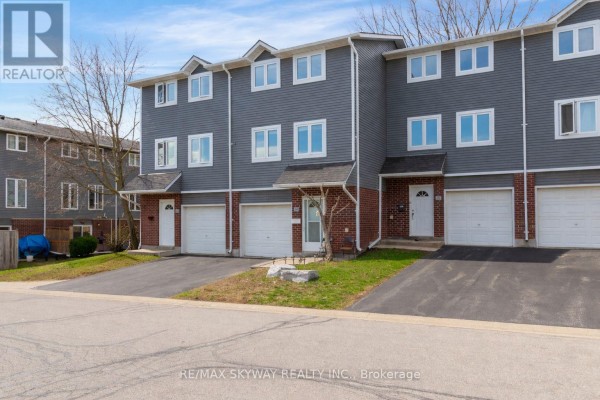 Front view of a townhouse complex with gray siding, brick accents, and attached garages. - B - 56 Harris Avenue, Brantford