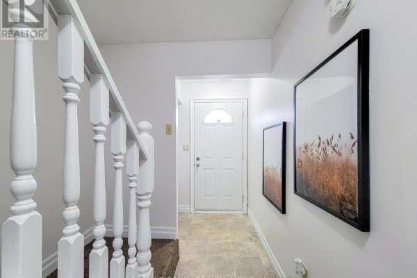 Hallway inside a townhouse with beige tile floor, carpeted stairs, and artwork on the wall. - B - 56 Harris Avenue, Brantford