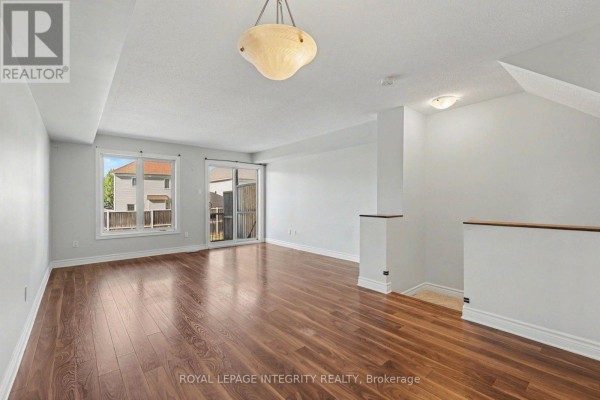 Bright living room with wood floors, white walls, and sliding glass doors to a deck. - B - 621 Chapman Mills Drive, Ottawa