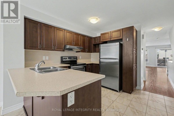Kitchen with dark wood cabinets, stainless steel refrigerator, and light countertops. - B - 621 Chapman Mills Drive, Ottawa