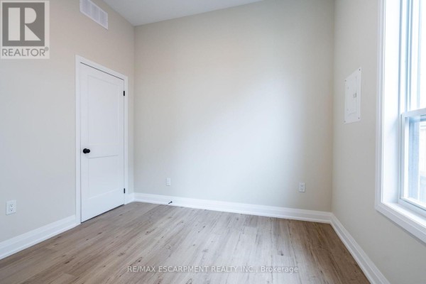 Empty room with light beige walls, white door, and wood-look flooring. - B - 728 Eleventh Avenue, Hamilton