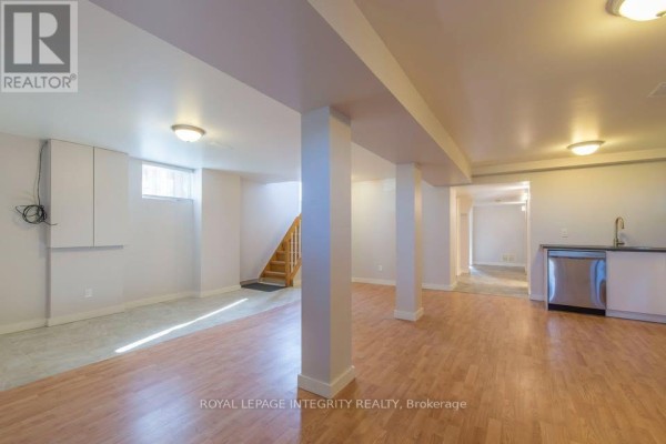 Basement living area with wood floors, white support columns, and a small kitchenette. - B - 892 Baseline Road, Ottawa