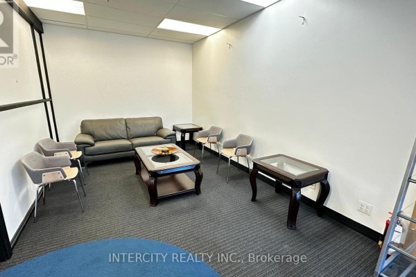 A waiting area in an office with a grey sofa, upholstered chairs, and dark wood coffee tables. - B - 99 Sante Drive, Vaughan