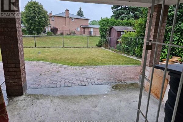 View from under a covered patio looking out to a grassy backyard with a fence and garden shed. - B - Basement - 16 Vineyard Court, Vaughan