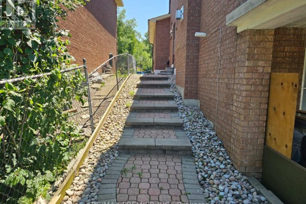 Stone and interlocking brick steps lead up alongside a brick house, bordered by gravel and greenery. - B - Basement - 16 Vineyard Court, Vaughan