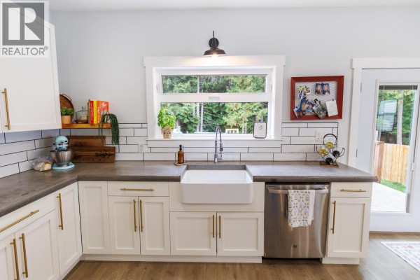 Kitchen sink area with a white farmhouse sink, gray countertop, dishwasher, and a window overlooking trees. - B 4005 Benner Street, Terrace