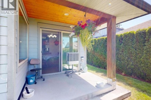 Covered concrete patio with a wooden ceiling, hanging flower baskets, and a sliding glass door. - B-6916 Abbotsford Street, Powell River