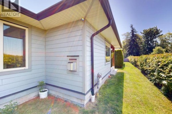 Corner view of the duplex with light blue siding, a large green hedge, and a small potted plant. - B-6916 Abbotsford Street, Powell River