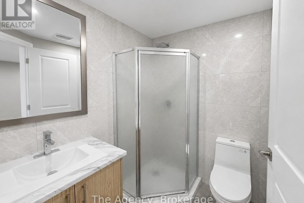 A compact bathroom featuring a corner glass shower, a white toilet, and a wood-toned vanity. - B1 - 143 Westchester Crescent, St  Catharines