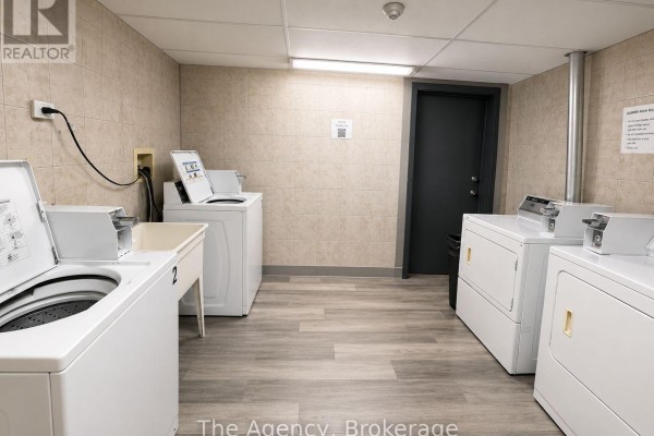 A communal laundry room with multiple white washing machines and dryers, and tiled walls. - B1 - 143 Westchester Crescent, St  Catharines