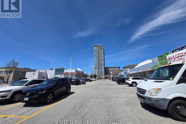 Wide view of a commercial plaza parking lot under a bright blue sky with clouds. - B10 - 4779 Steeles Avenue E, Toronto