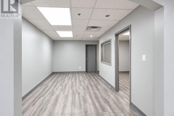 Hallway with light gray walls, gray doors, and a window with blinds. - B101 - 7155 Woodbine Avenue, Markham