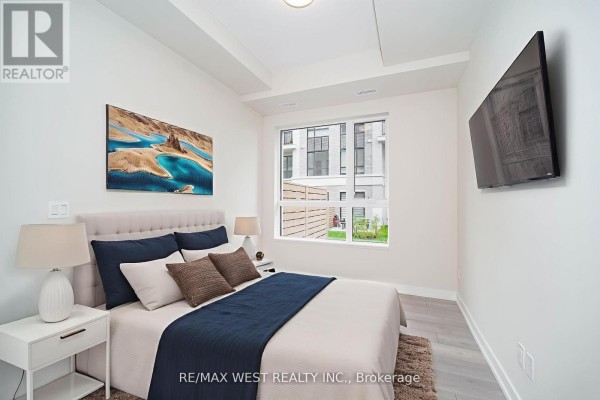 A bedroom featuring a bed with navy and white bedding, a nightstand, and a window with a street view. - B103 - 65 Saigon Drive, Richmond Hill