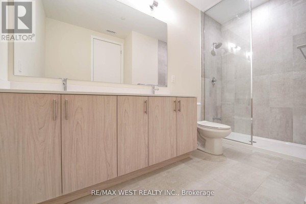 A spacious bathroom with a double vanity, light wood cabinets, and a glass-enclosed shower with grey tiles. - B103 - 65 Saigon Drive, Richmond Hill