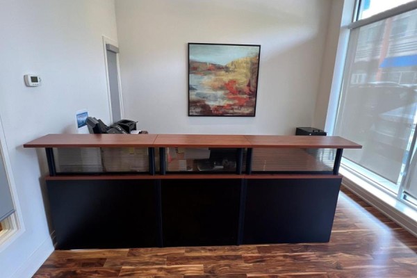 Close-up of the reception desk with dark base, wooden countertop, and office equipment. - B108 - 11685 Yonge Street, Richmond Hill
