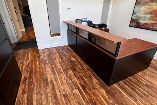 Reception desk with L-shaped wooden countertop and dark base on a wood-patterned floor. - B108 - 11685 Yonge Street, Richmond Hill