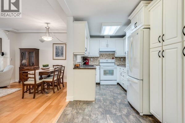 Interior view of a dining area with a wooden table and chairs, adjacent to a white kitchen. - B207 4821 53 Street, Ladner