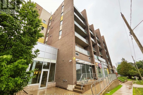 Glass and brick entrance to an apartment building with outdoor paved area. - B303 - 62 Balsam Street, Waterloo