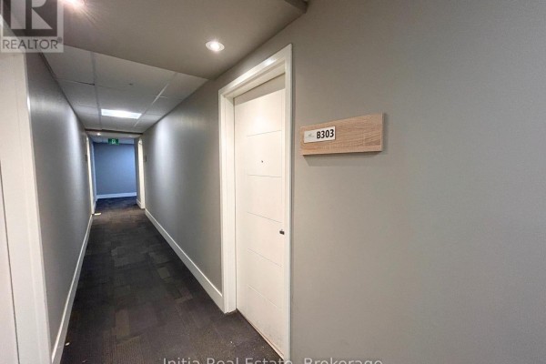 Apartment hallway with dark carpet, gray walls, and a white door labeled B303. - B303 - 62 Balsam Street, Waterloo
