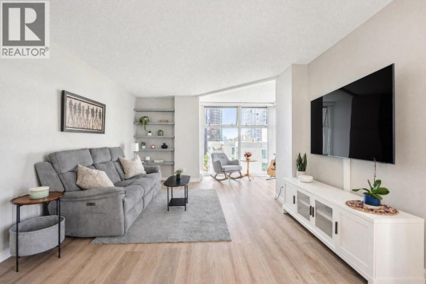 Living room with gray sofa, television on white media console, and a rocking chair by the window. - B901 1331 Homer Street, Vancouver