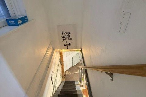 Narrow staircase leading down with a sign reading 'Please watch your step'. - Back - 15 Dunlop Street W, Barrie