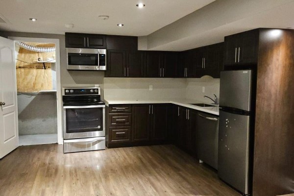 Basement kitchen with dark wood cabinets, stainless steel appliances, and wood-look flooring. - Basement - 118 Earlsbridge Boulevard, Brampton