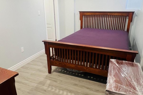 Basement bedroom featuring a wooden bed frame with a purple comforter and a wooden nightstand. Grey walls and light grey vinyl flooring. - Basement - 121 Bonnieglen Farm Boulevard, Caledon
