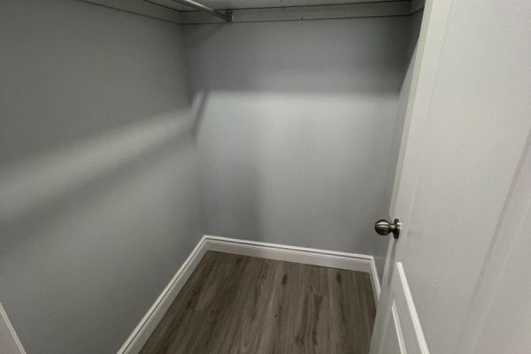 Empty walk-in closet with grey walls, white trim, and light grey vinyl flooring. A white door with a silver knob is visible. - Basement - 121 Bonnieglen Farm Boulevard, Caledon