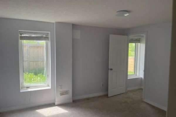Bright basement bedroom with two windows, beige carpet, and light grey walls. - Basement - 130 Vantage Loop, Newmarket