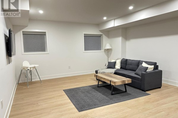 Living room with charcoal sofa, wooden coffee table, and a high chair on a dark rug. - Basement - 1351 Northmount Avenue, Mississauga