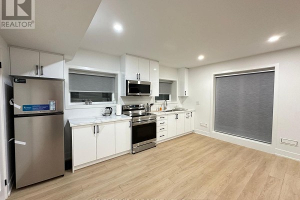 Kitchen with white cabinets, stainless steel appliances, and a large window with blinds. - Basement - 1351 Northmount Avenue, Mississauga