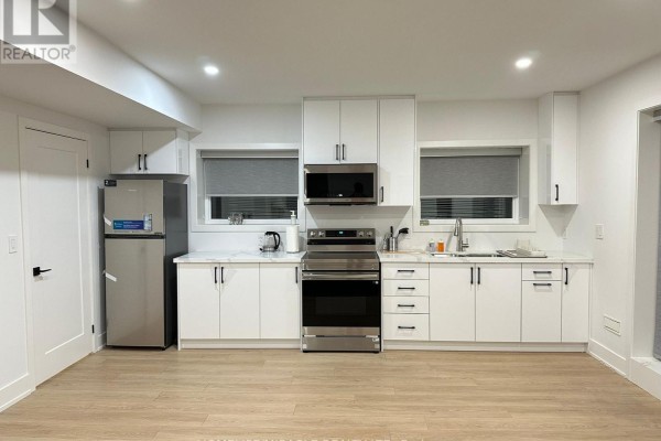 Full kitchen view with white cabinetry, stainless steel appliances, and light wood flooring. - Basement - 1351 Northmount Avenue, Mississauga