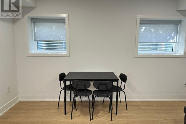 Dining area with a black table and four chairs against a white wall with two windows. - Basement - 1351 Northmount Avenue, Mississauga