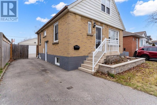 Close-up of the side of a light brown brick house with a black door and small windows. - Basement - 144 Taylor Avenue, Hamilton