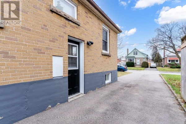 View of the side of a brick house showing a black door, driveway, and neighboring houses. - Basement - 144 Taylor Avenue, Hamilton