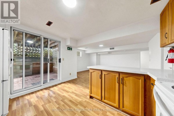 Basement kitchen and living area with wood laminate flooring, white walls, and a sliding glass door. - Basement - 156 Centennial Road, Toronto