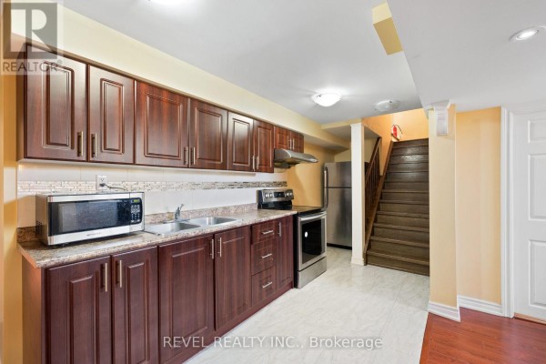 Basement kitchen with dark wood cabinets, granite countertops, stainless steel appliances, and stairs leading up. - Basement - 16 Terrance Drive, Markham