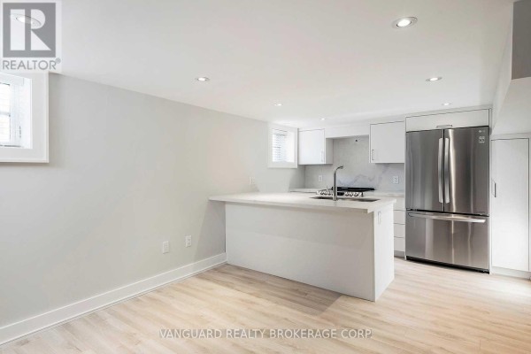 A modern basement kitchen with white cabinets, an island, and stainless steel appliances. - Basement - 187 Brooke Avenue, Toronto