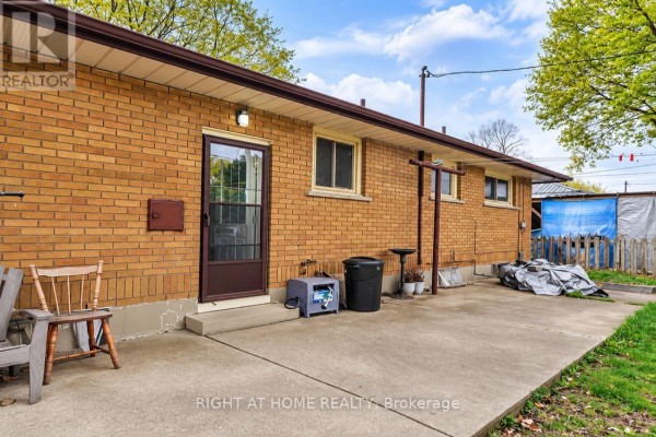 Back exterior of a brick house with a concrete patio and a brown door. - Basement - 200 Renfro Crescent, London South